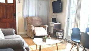 Ein Wohnzimmer mit Holzboden, einer Couch, einem Couchtisch, einem Fernseher und einem Sessel.