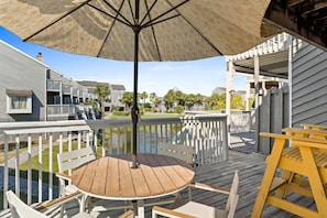 A wooden deck with a round table and chairs, a large umbrella, and a view of residential buildings. - Cozy Dog-Friendly Cottage · Steps to Gulf Beach (Port St. Joe)