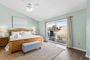 A bedroom with a bed, bedside tables, a bench, a ceiling fan, and a view of a deck and buildings. - Cozy Dog-Friendly Cottage · Steps to Gulf Beach (Port St. Joe)