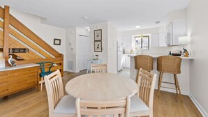 A modern kitchen with white cabinets, a dining area with a round table and wooden chairs, and a staircase with wooden railings. - Cozy Dog-Friendly Cottage · Steps to Gulf Beach (Port St. Joe)