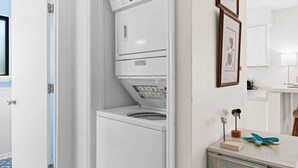A compact laundry room with a front-loading washer and dryer, a small cabinet with decorative items, and a mirror above the counter. - Cozy Dog-Friendly Cottage · Steps to Gulf Beach (Port St. Joe)