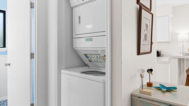 A compact laundry room with a front-loading washer and dryer, a small cabinet with decorative items, and a mirror above the counter. - Cozy Dog-Friendly Cottage · Steps to Gulf Beach (Port St. Joe)