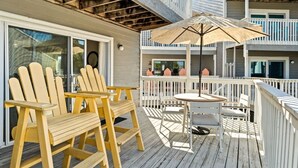 A wooden deck with Adirondack chairs and a table, a white umbrella, and a balcony with railings. - Cozy Dog-Friendly Cottage · Steps to Gulf Beach (Port St. Joe)