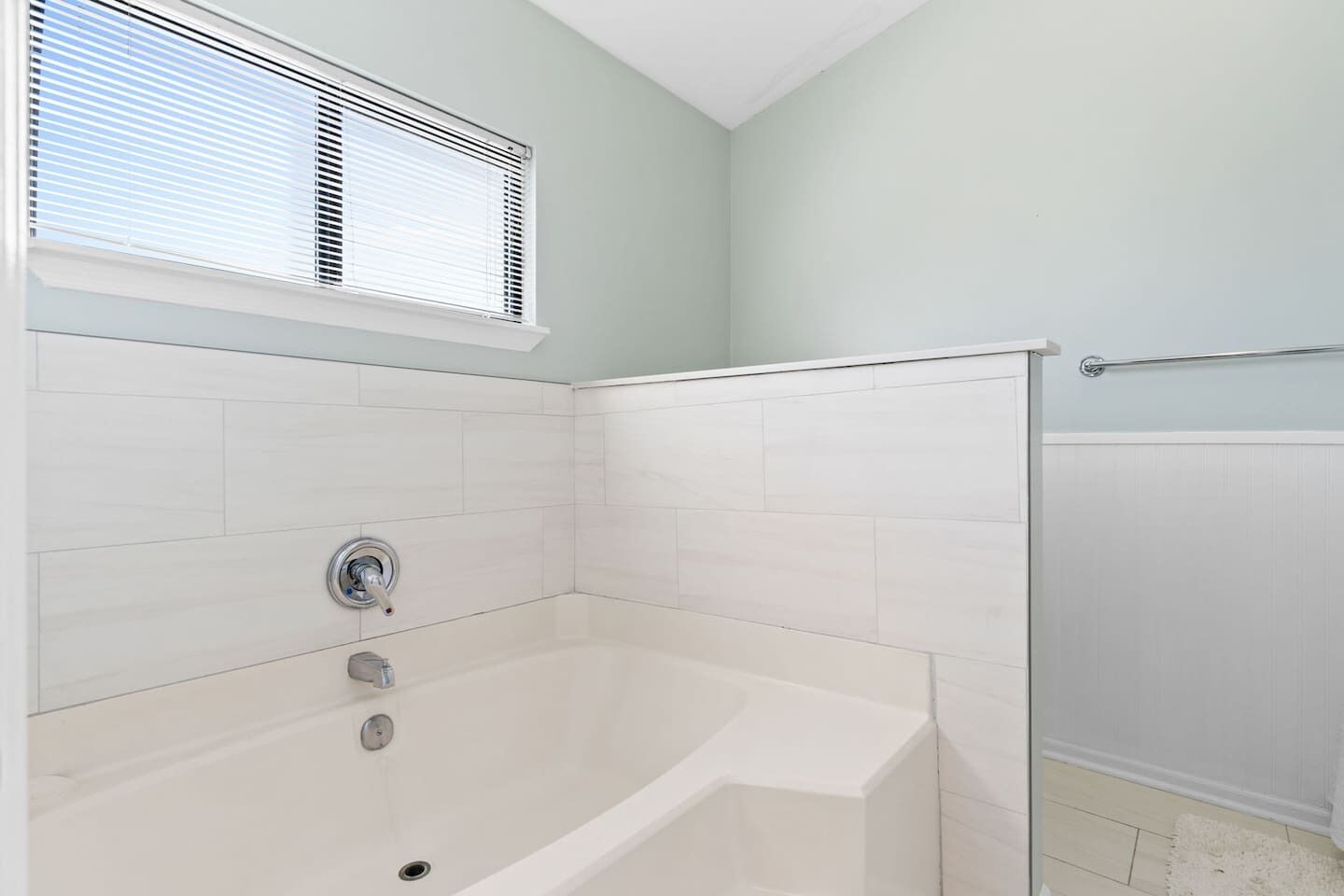 A bathroom with a bathtub, a shower, and a window with blinds.