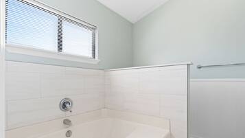 A bathroom with a bathtub, a shower, and a window with blinds.
