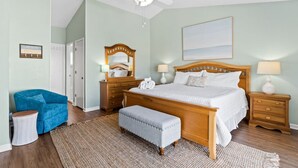 A bedroom with a bed, nightstands, a chair, a bench, a ceiling fan, a mirror, and a door. - Cozy Dog-Friendly Cottage · Steps to Gulf Beach (Port St. Joe)