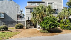 A residential building with a gated entrance, a small garden with palm trees, and a clear sky. - Cozy Dog-Friendly Cottage · Steps to Gulf Beach (Port St. Joe)