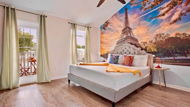 Una camera da letto con un letto, una ventola a soffitto, una finestra con tende e un murale della Torre Eiffel.