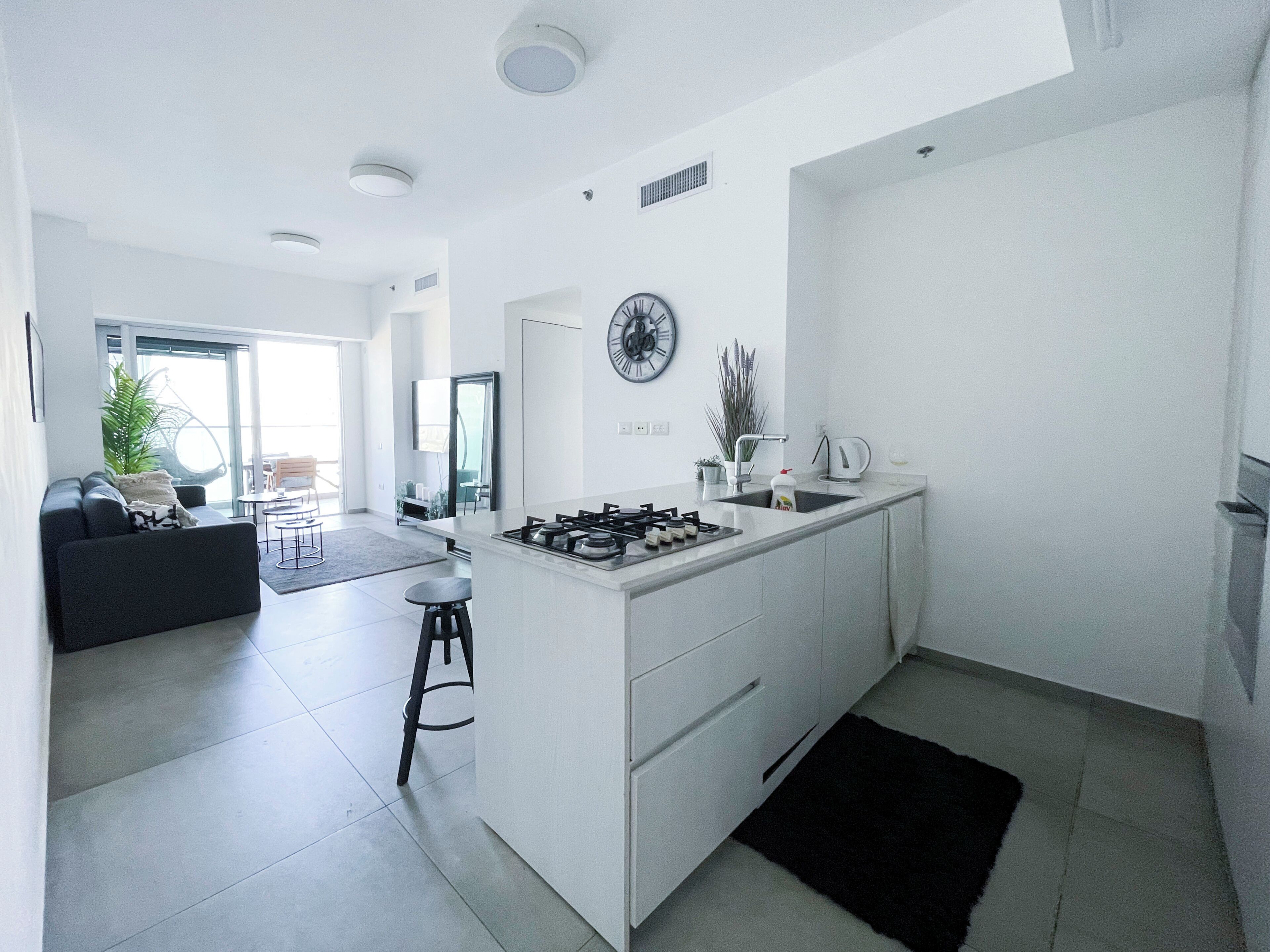 A modern kitchen with a central island, a dining area with a sofa and chairs, and a large window providing natural light.