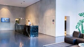 Een moderne lobby met een marmeren receptiebalie, een bank en een grote plant.