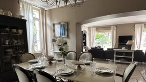 Un comedor con candelabro, mesa de comedor preparada para seis personas y vista al salón con televisor.