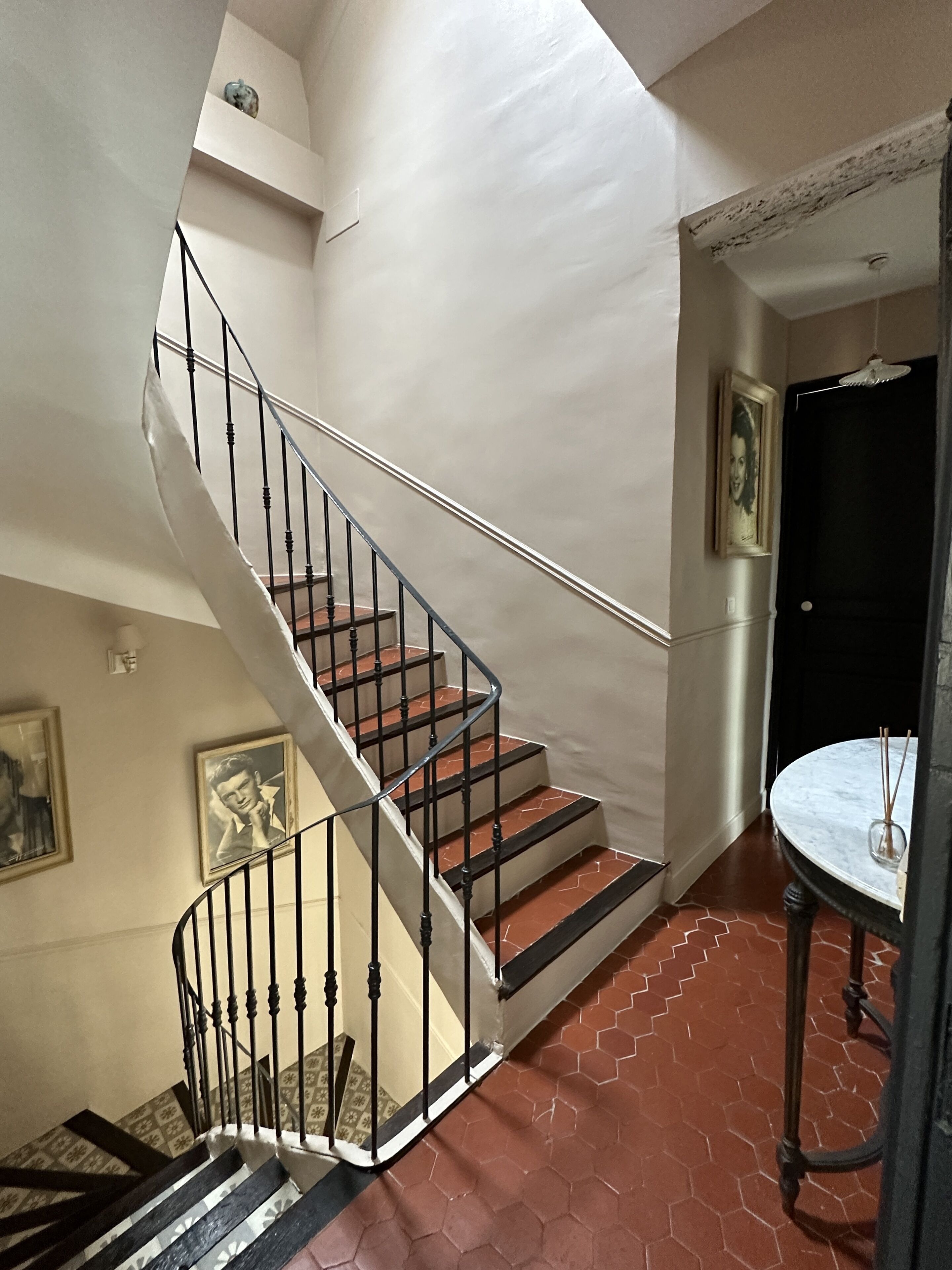 A spiral staircase with a black railing, a round table with a vase, and hexagonal patterned flooring.