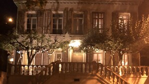 Un edificio con una escalera que conduce a una entrada porticada, rodeado de árboles e iluminado con luces colgantes.