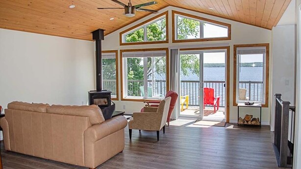 A spacious living room with a high ceiling, large windows, a fireplace, and a view of a body of water.