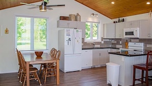 A kitchen with white cabinets, a central island, a ceiling fan, and a dining area with wooden chairs and a table.
