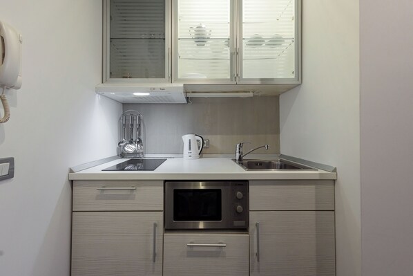 A compact kitchen with a built-in oven, a kettle, and a sink.