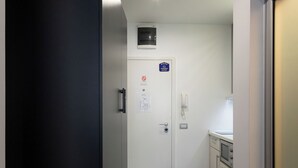 Un pasillo con una puerta negra, una puerta blanca que tiene un teléfono y un cartel, y una pequeña área de cocina con armarios y una encimera.