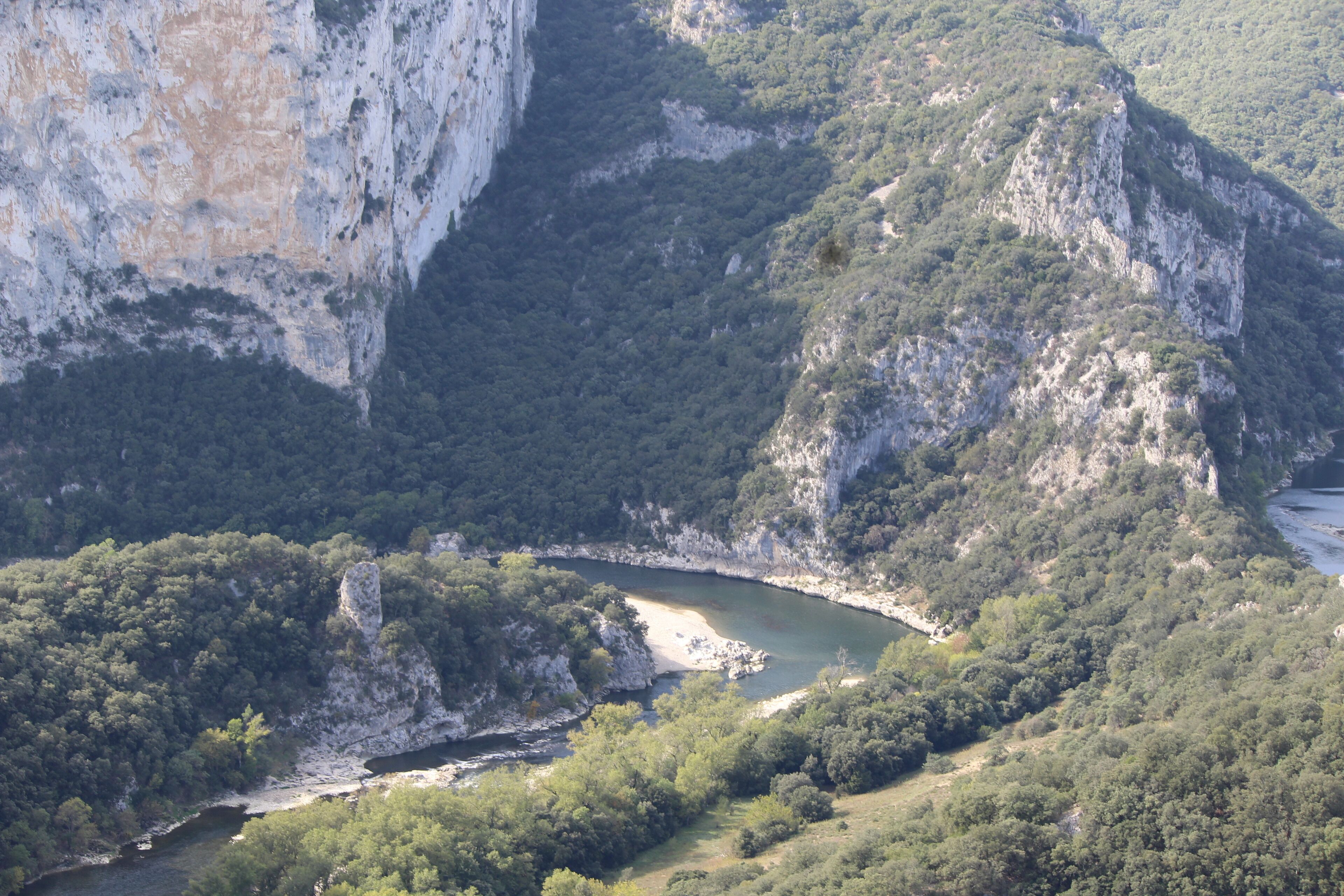 A mountainous landscape with a river, dense forest, and rocky cliffs.