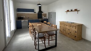 A modern kitchen with a dining area, featuring a wooden table, chairs, a black pendant light, and a built-in oven. - Gîte « Les Oliviers » Dans Mas Typiquement Ardéchois - 6 Personnes (Saint-Sauveur-de-Cruzières)