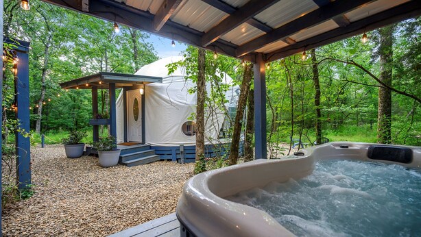 Ein Whirlpool, eine überdachte Sitzgelegenheit und ein Zelt in einer bewaldeten Landschaft.