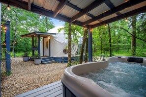 A hot tub, a covered seating area, and a tent in a forested outdoor setting.