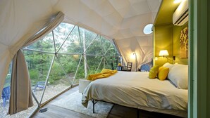 Ein Zeltunterstand mit einem Bett, einem Schreibtisch und Blick auf den Wald.