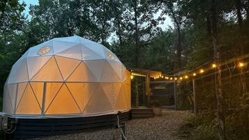 A geodesic dome tent with a "HAPPY PLACE" sign, surrounded by trees and string lights.