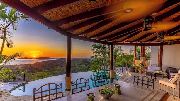A covered outdoor seating area with a pool, overlooking a scenic landscape and sunset. - Papagayo Ocean View Luxury Villa (Carrillo Guanacaste)