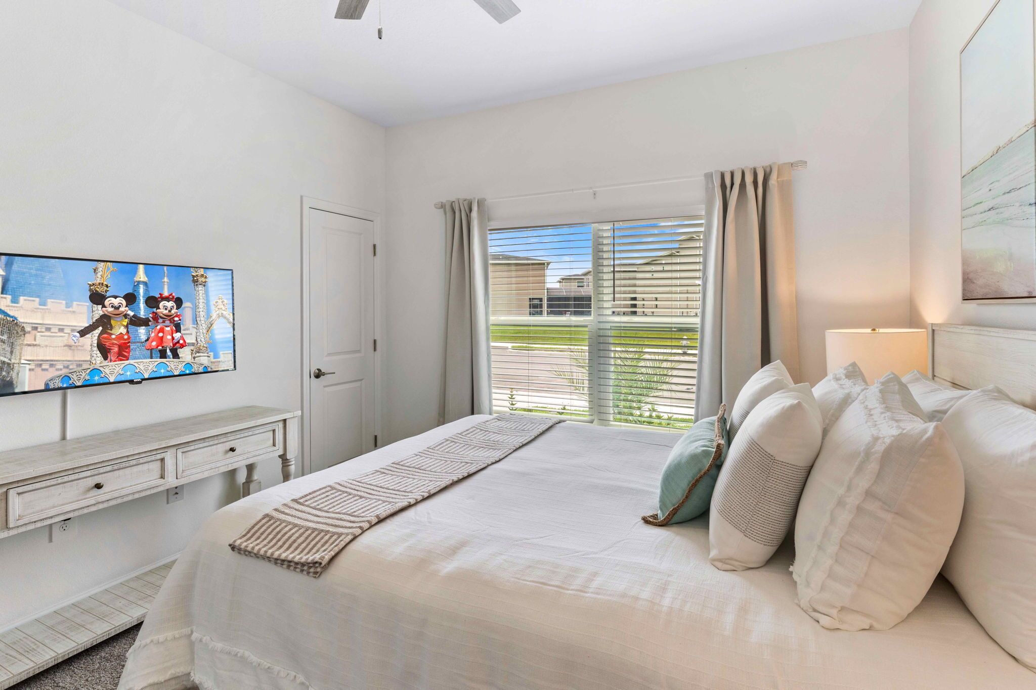 Une chambre à coucher avec un lit, un téléviseur fixé au mur, une fenêtre avec des rideaux et une vue sur l’extérieur.