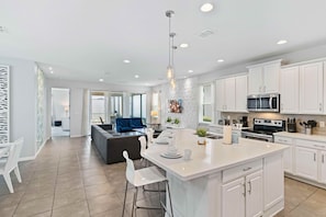 A modern kitchen with white cabinetry, a central island, and a dining area with a blue sofa.