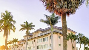 Ein mehrstöckiges Hotel mit einer hellrosa Fassade, zahlreichen Balkonen und einem gepflegten Rasen mit Palmen.