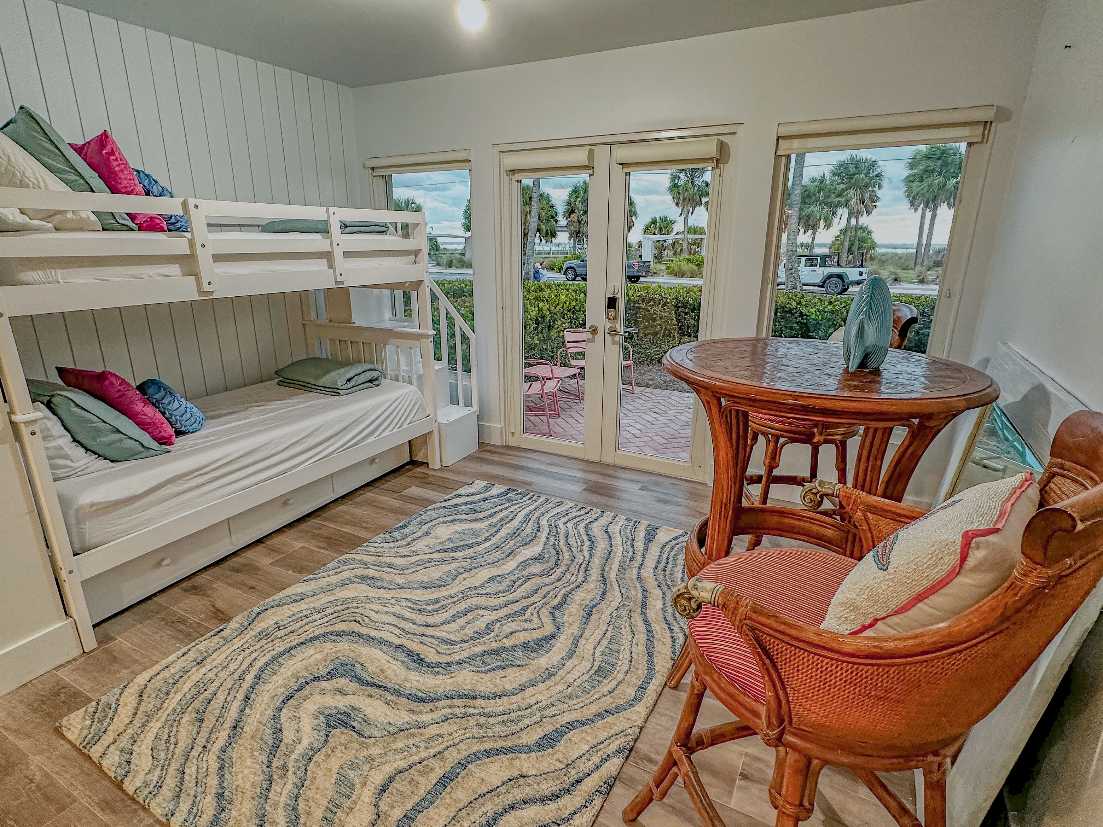 A room with bunk beds, a round wooden table, wicker chairs, and a patterned rug.