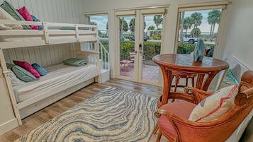 A room with bunk beds, a round wooden table, wicker chairs, and a patterned rug.