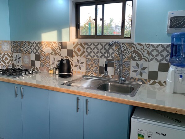 A kitchen with a gas stove, a kettle, a sink, and a window. - Fully equipped cabin (Isla de Pascua)