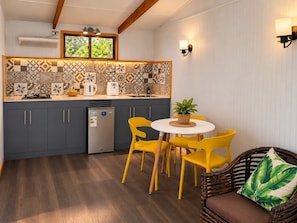 A compact kitchen with a central island, a dining area with yellow chairs, and a wicker sofa with a green leaf pillow.