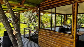 Une cabane en bois dotée d’une terrasse, de grandes fenêtres et offrant une vue sur un jardin luxuriant.