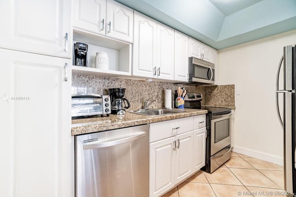 A kitchen with white cabinets, a granite countertop, a dishwasher, a microwave, a stove, and a refrigerator.