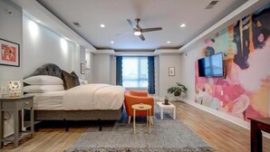 Een moderne slaapkamer met een bed, een plafondventilator, een televisie en een kleurrijk abstracte muur.