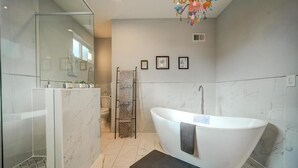 Een moderne badkamer met een vrijstaand bad, een douchecabine met glazen wanden en een handdoekrek.