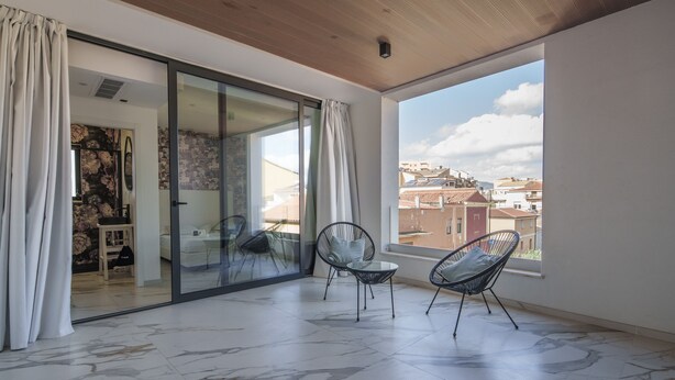 A balcony with two chairs, a sliding glass door, and a view of buildings.