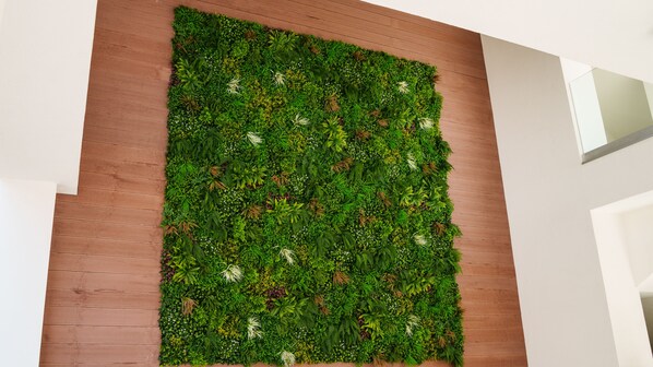 Pared vegetal vertical con diversas plantas verdes y pequeñas flores blancas.