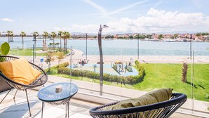 A balcony with wicker chairs and a glass table overlooking a marina with boats, a playground, and a landscaped area. - Welcomely - Seamphony Superior Room (Olbia)
