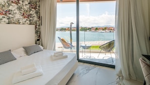 A hotel room with a bed, a view of the sea, and a balcony with chairs. - Welcomely - Seamphony Superior Room (Olbia)