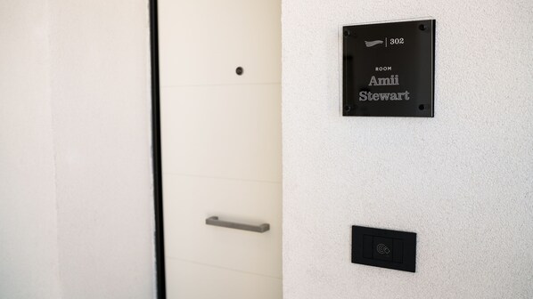 A room number plaque on a textured wall, a door with a handle, and a control panel below it.