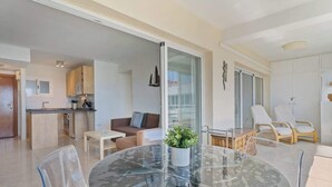 Ein modernes Wohnzimmer mit Glastisch, transparenten Stühlen, einem braunen Sofa und einer Topfpflanze.