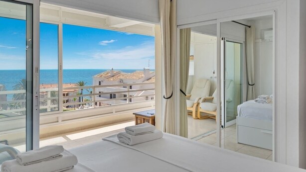 Ein Hotelzimmer mit großem Balkon, einem Bett mit Handtüchern, einem Stuhl und einer Glastür zu einem Duschbereich.
