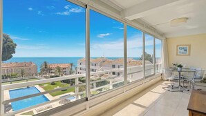Ein geräumiger Balkon mit großen Fenstern, Blick auf einen Pool und die Küste.