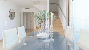 A dining area with a glass table, white chairs, and a vase with candles.