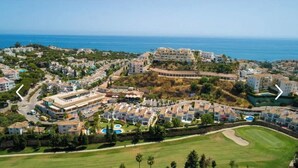 An aerial view of a coastal resort with multiple buildings, a golf course, and a large body of water in the background.