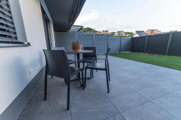 A patio with a table and chairs, a potted plant, and a view of houses in the background.